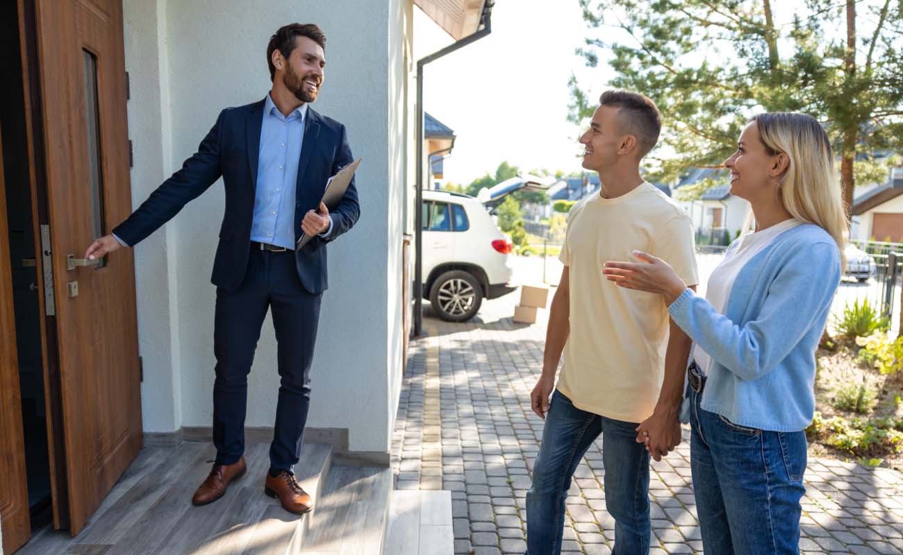Male Realtor outside a house welcoming man and woman.