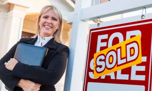 A realtor next to a real estate sign with a sold sign on it.